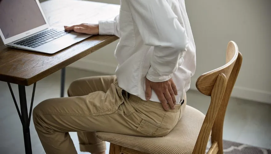 um homem com dor nas costas sentado em uma cadeira