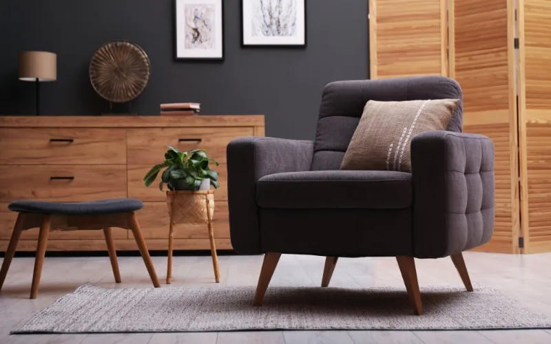 Poltrona moderna cinza-escura com mesa lateral de madeira e plantas, perfeita para um cantinho de leitura.