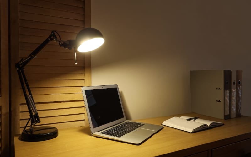 Warm home office lighting illuminating a laptop and notebook on a wooden desk