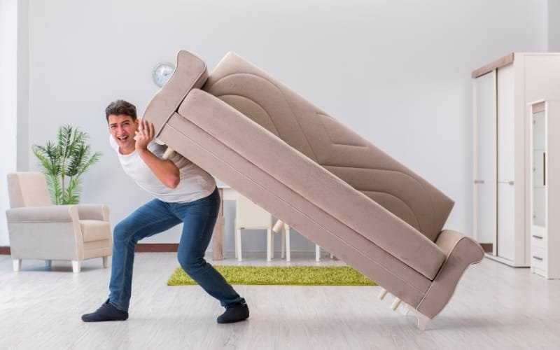 Man lifting a large sofa in a bright living room, demonstrating heavy furniture moving